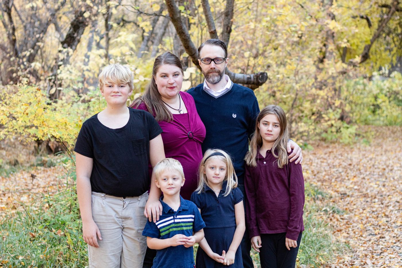 The family standing together outdoors among yellow autumn leaves